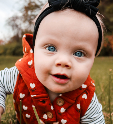 An angelic baby with bright blue eyes shining like sapphires, wrapped in a cozy red vest